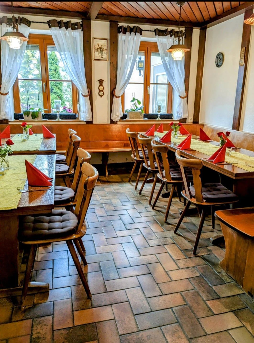 Gaststube mit gedeckten Holztischen, roten Servietten und weißen Gardinen