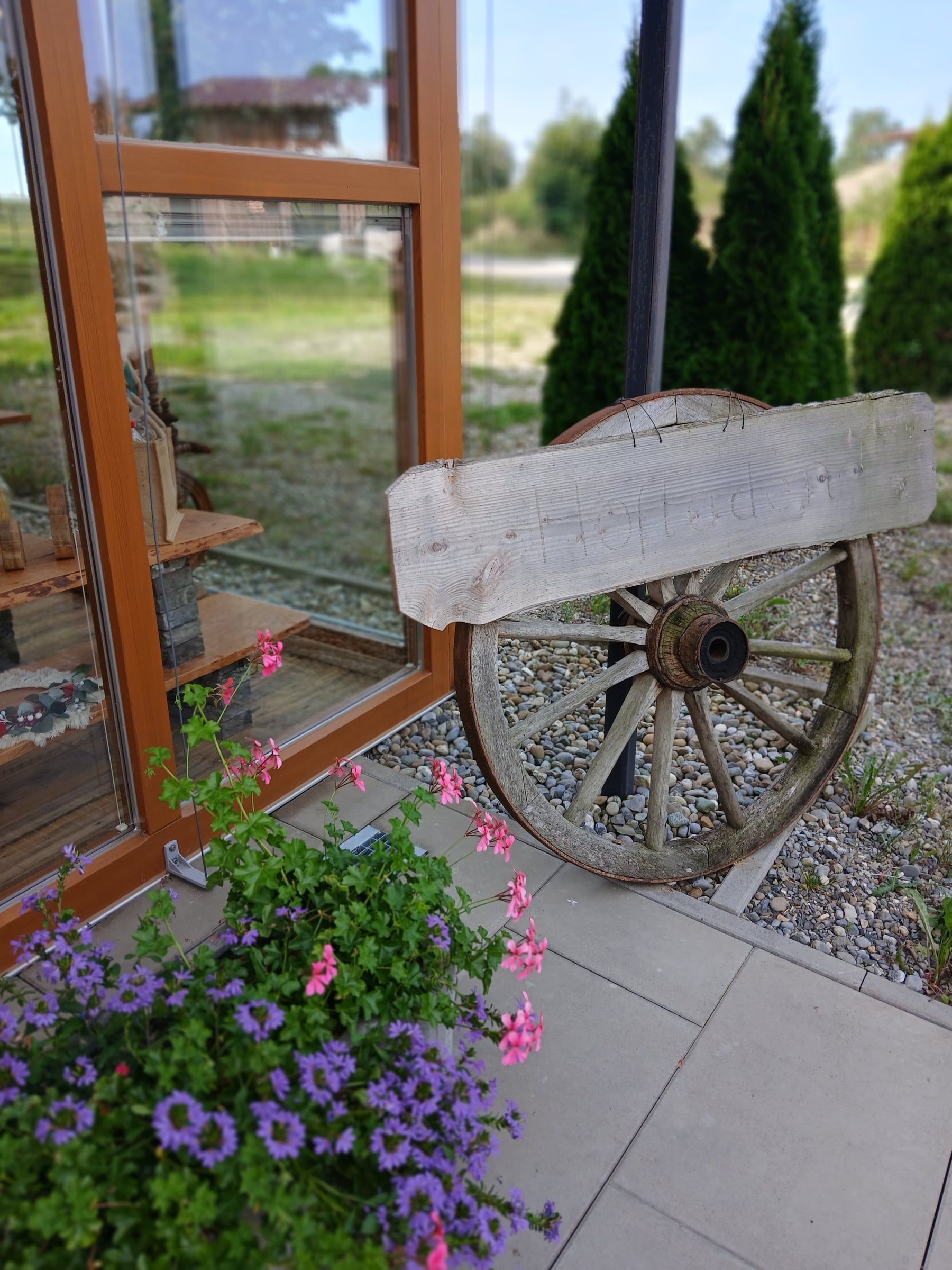 Altes Wagenrad mit Holzschild „Hofladen“ und Blumen vor dem Eingang