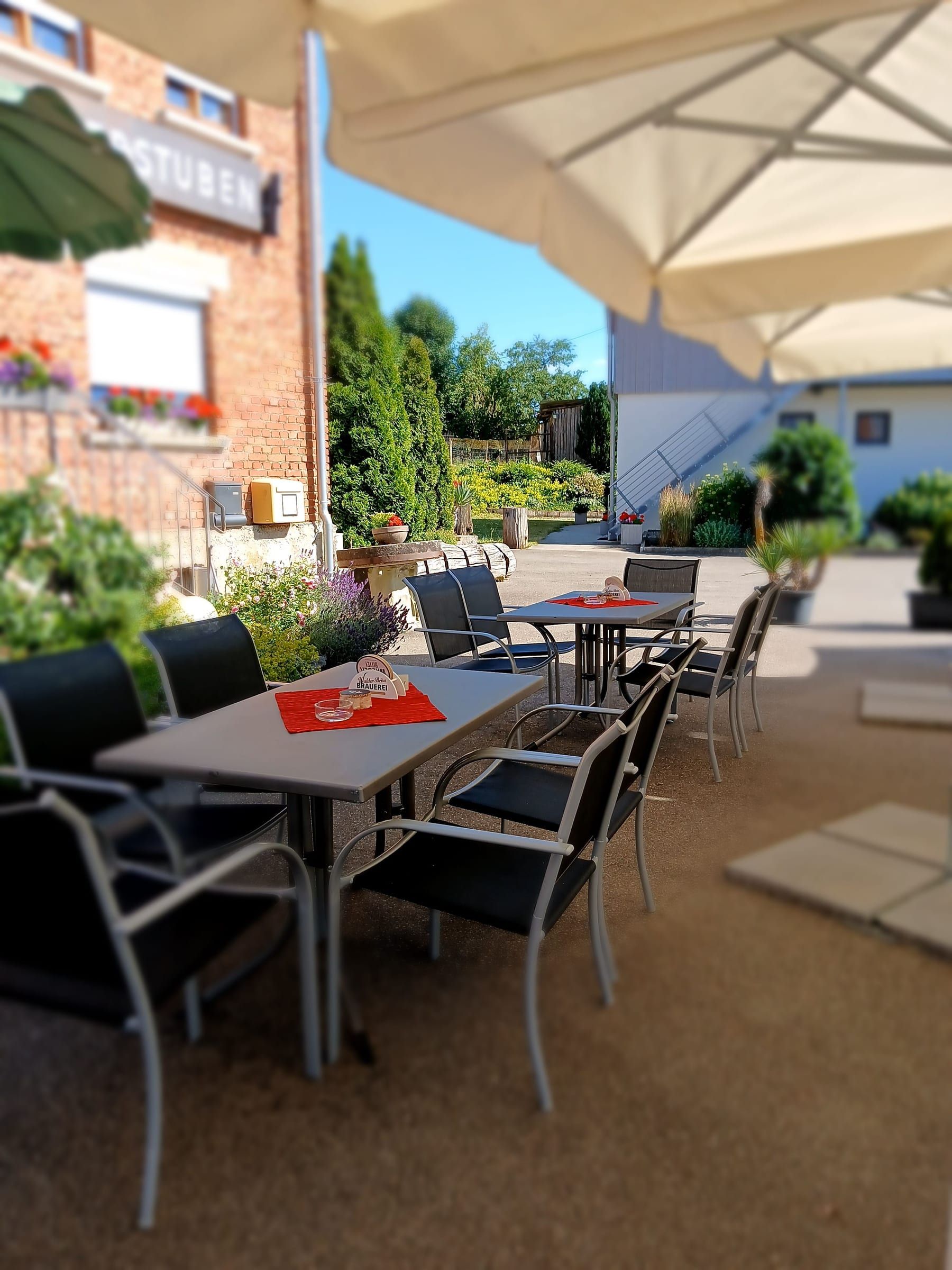 Terrasse mit Sonnenschirm, Tischen und Blumen vor dem Gasthof