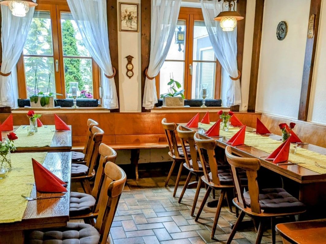 Gaststube mit gedeckten Tischen, roten Servietten und weißen Gardinen