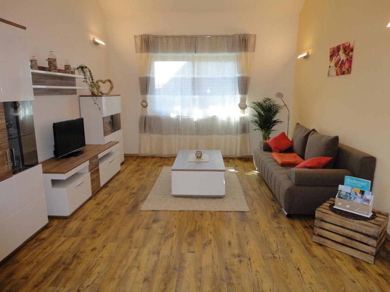 Wohnbereich mit grauer Schlafcouch, Wohnwand, Fernseher und großem Fenster